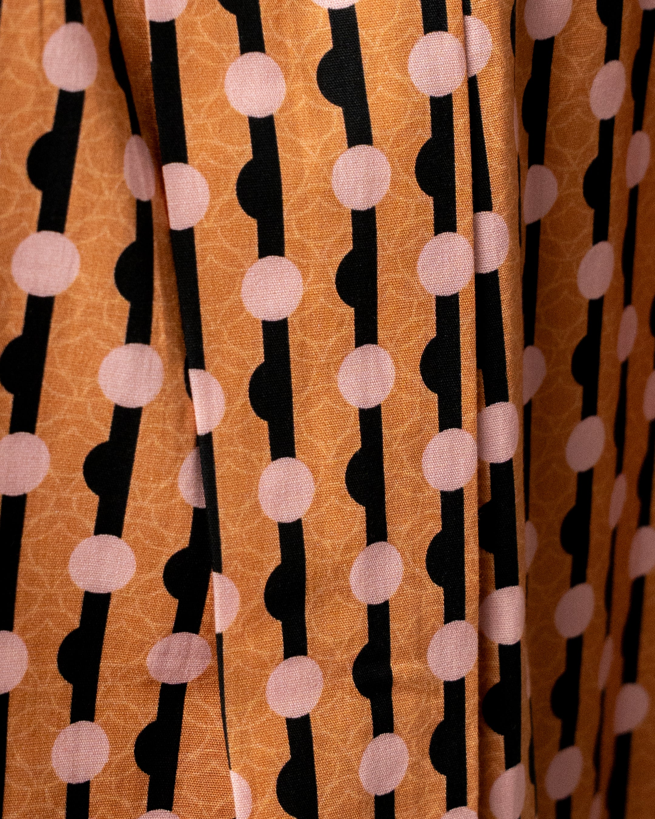 Patterned fabric with black lines and pink circles on an orange background