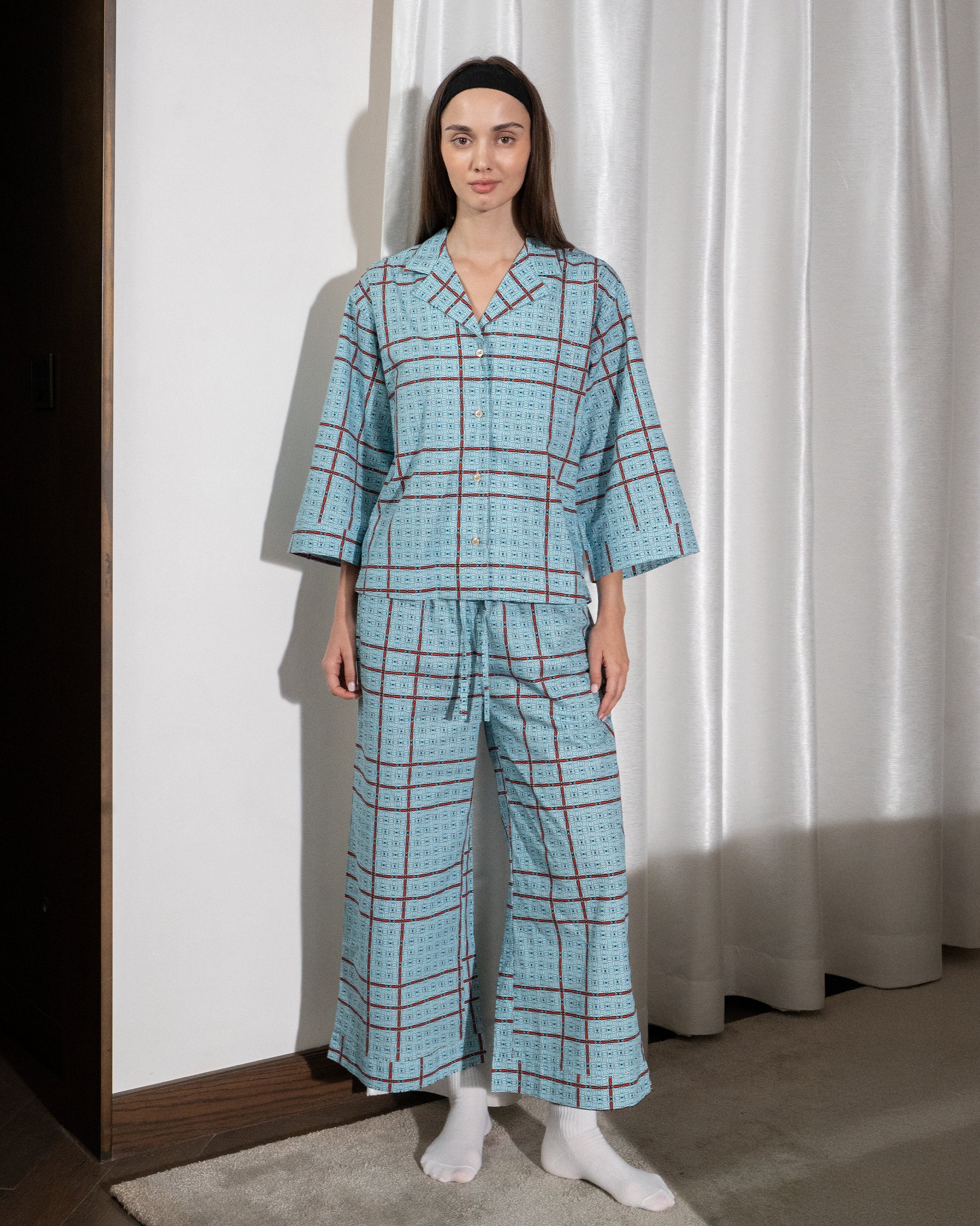 Woman wearing a blue plaid pajama set standing against a white curtain.