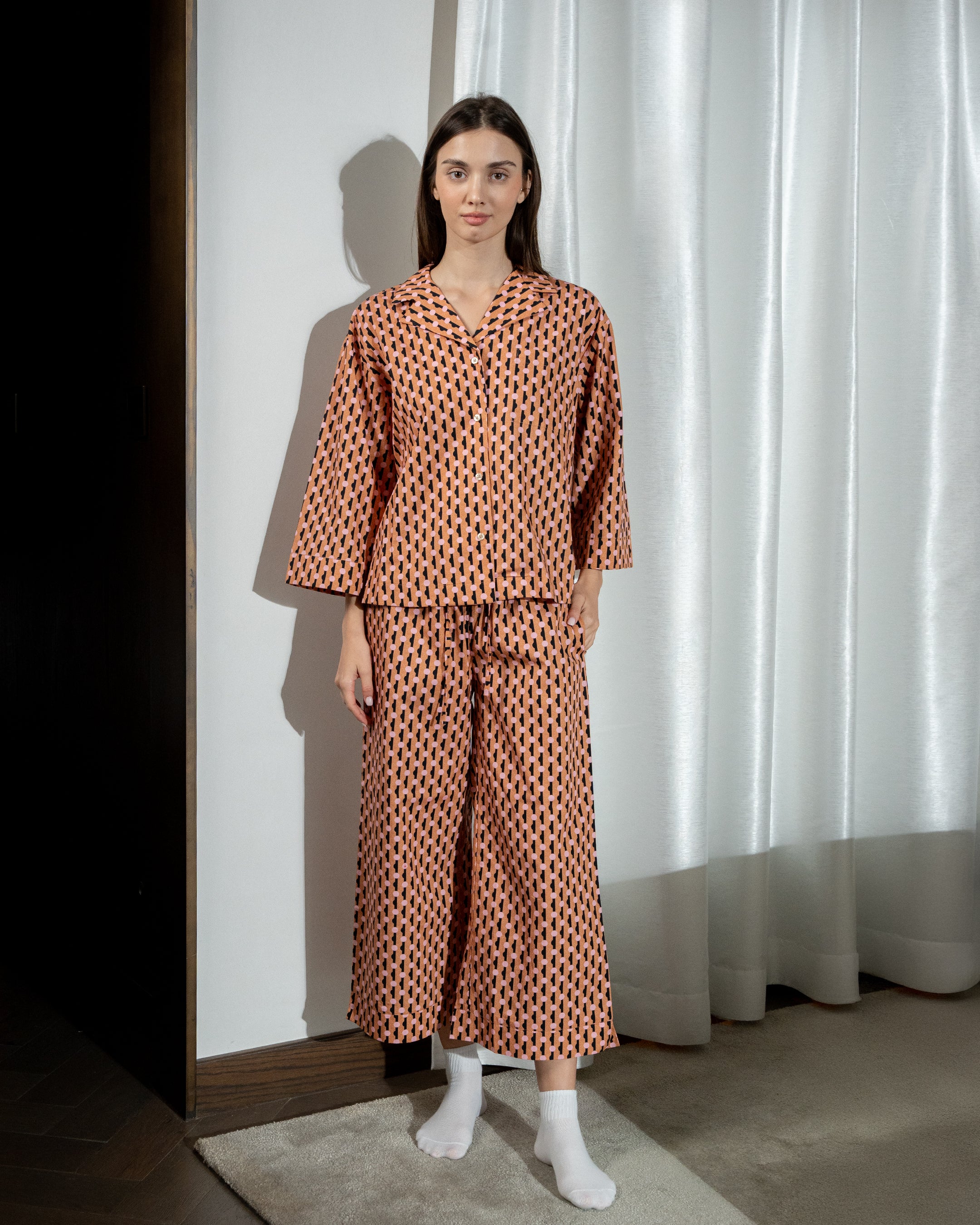 Woman wearing a patterned outfit standing against a white curtain.