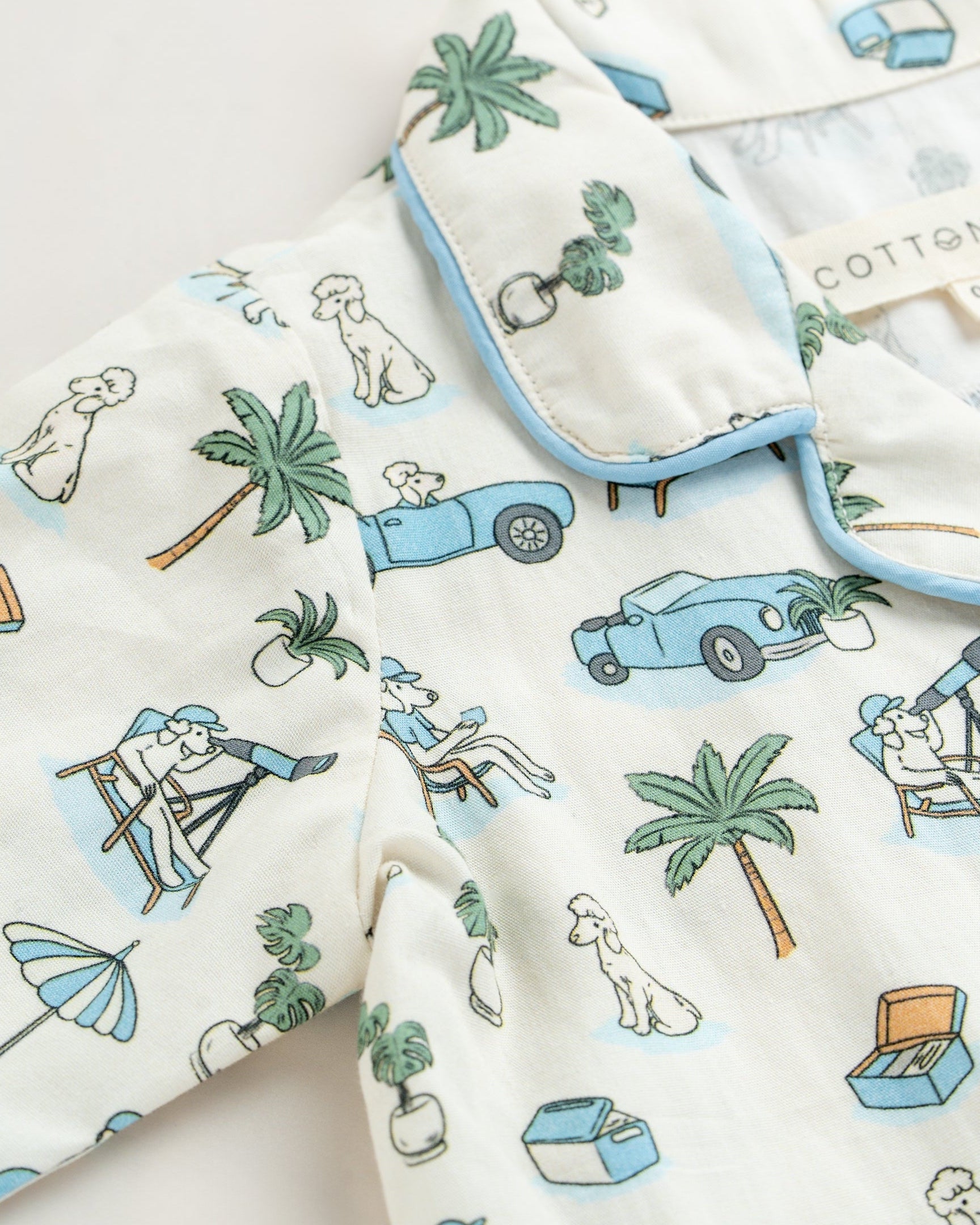 Baby clothing with a tropical pattern featuring palm trees, cars, and people on a white background.